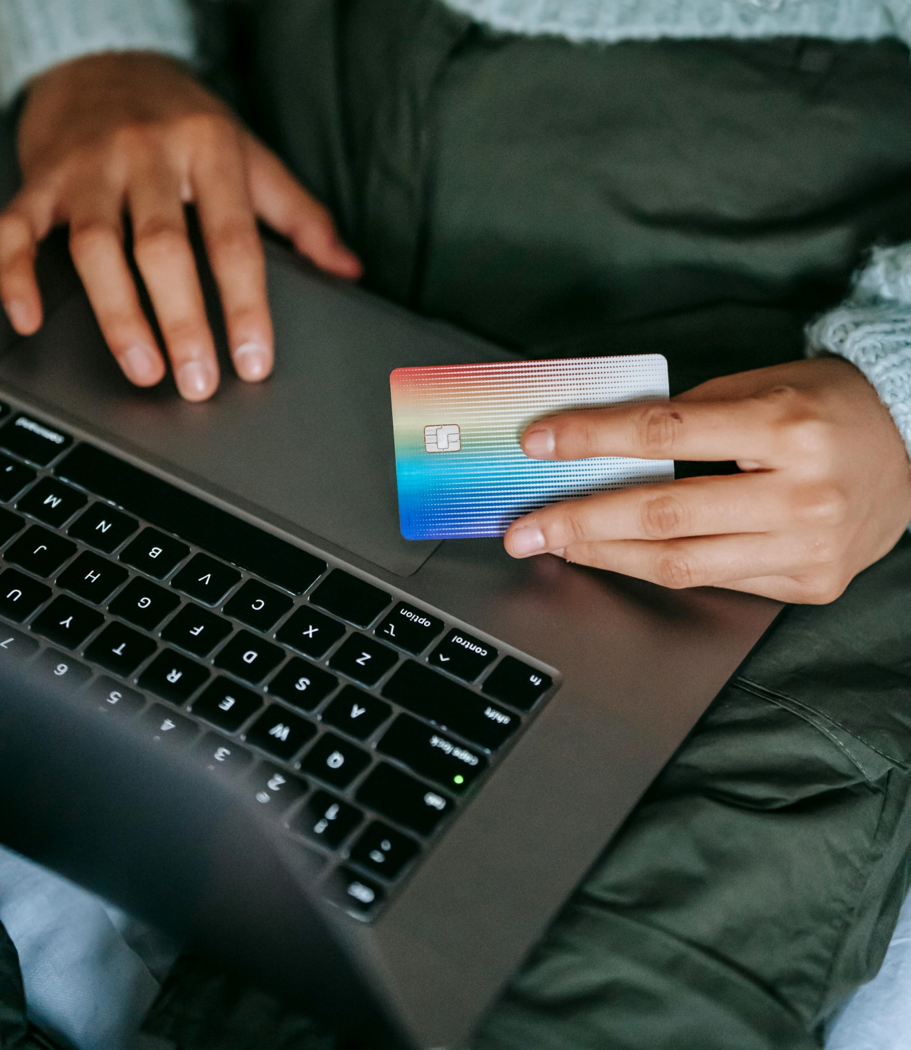 A cropped woman wearing a sweater holding a payment card in hand