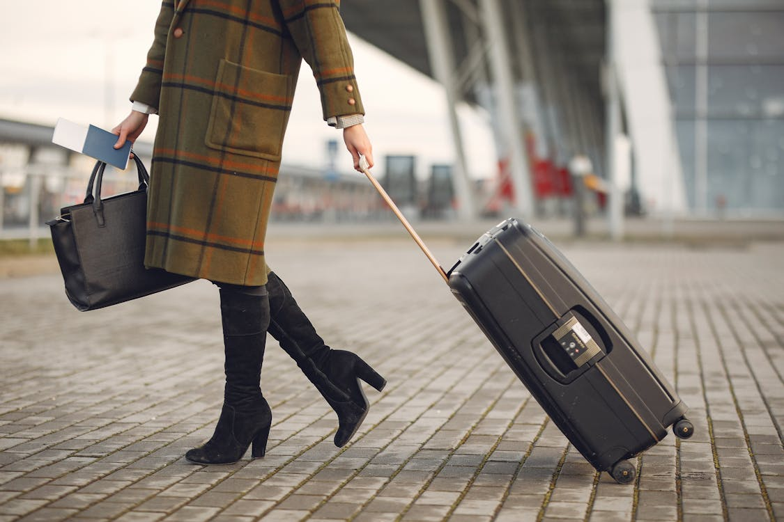 A person dragging their travel bag and holding a passport in the other hand